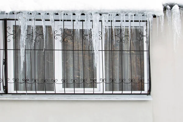 Frozen ice hanging over the window of a residential building with windows on the balcony is dangerously humiliated by passersby. Icicles over the window of the apartment in the winter in a row