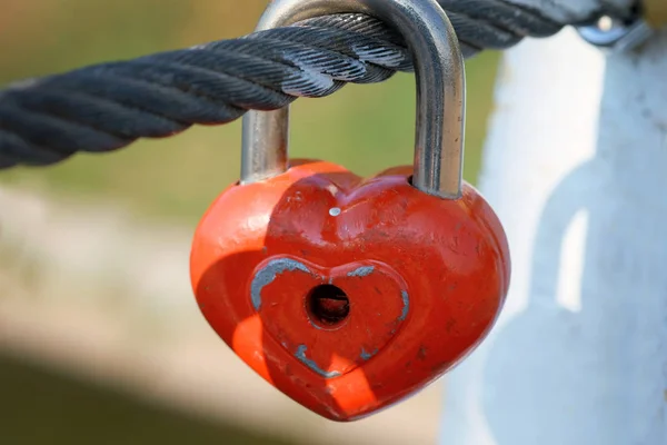 Red lock hang on a cable on a bridge. Symbol of eternal love and fidelity metal heart-shaped lock on the bridge close-up. Wedding traditions.