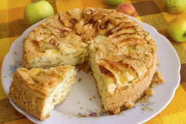 homemade pastries for tea, apple pie, biscuit dough. cut pie with apples on a plate on a yellow tablecloth background.