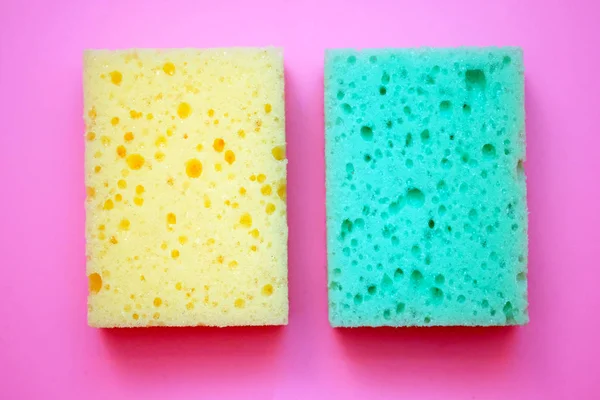 Green and yellow foam sponge for washing dishes. Soft washcloths on a pink background top view.