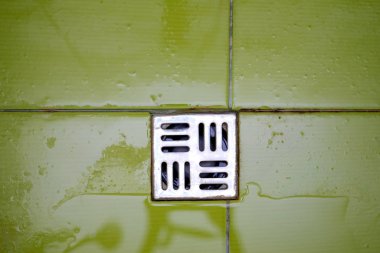 Shower grate on the floor. Top view draining hole in the bathroom. Wet green tiles and metal floor grille.
