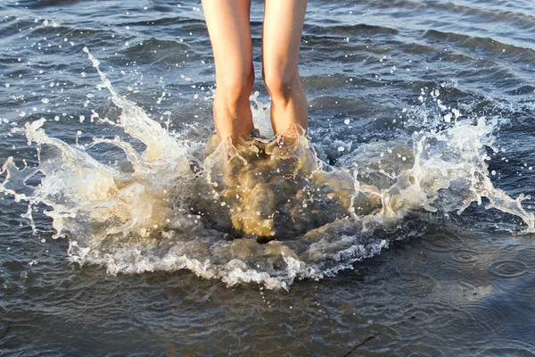 A young girl jumps into the water, splashes against the water, long tanned legs