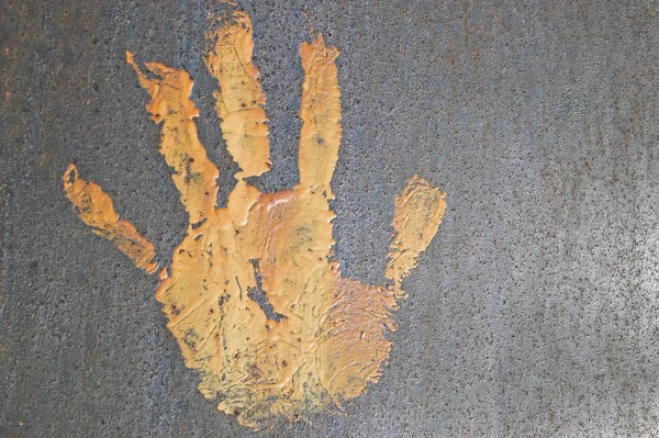 the imprint of a hand with an oil paint of orange color on an iron rusty surface