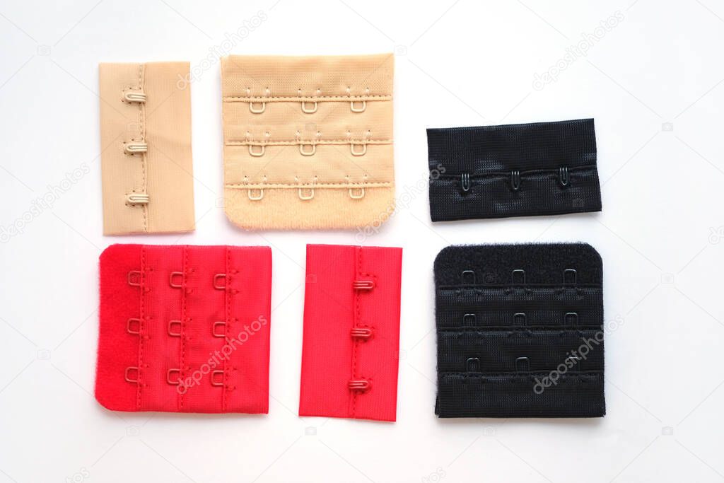 Red, black and beige clasp for bra and corset with three hooks on a fabric basis. Colored bra clasps on a white background top view. Accessories for sewing underwear.