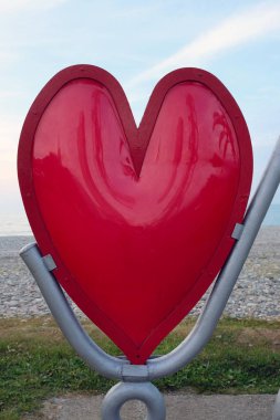 Red heart made of metal close-up on the beach. Symbol of love for Valentine's Day.