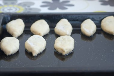 Fırın tepsisindeki turtalar pişirilmeye hazır. Çörek biçimli hamur siyah bir pişirme tepsisinin üzerinde yatıyor. Ev yapımı pişirme işlemi.