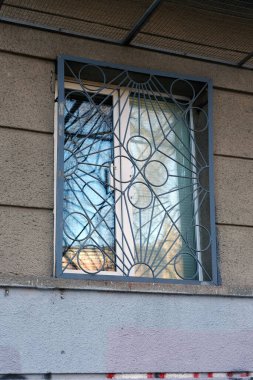 Gri metal parmaklıklı pencere. Zemin katta kıvrımlı düz kafesli plastik bir pencere var..