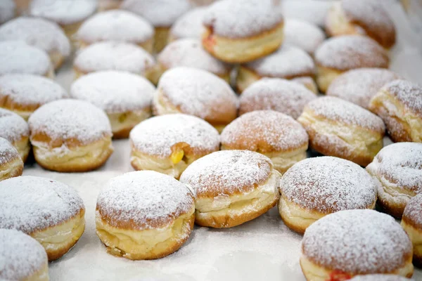 Round donuts sprinkled with white icing sugar with fruit jam. Homemade stuffed donuts on a parchment covered table. Sweet baking department in the store.