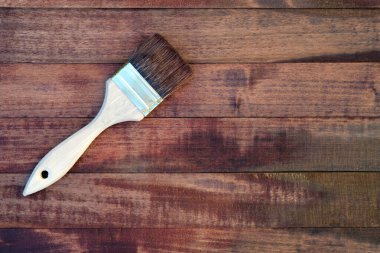 Lekeli üst manzara ile kaplı tahta tahtalar. Ahşap saplı bir fırça ve boyalı ahşap kalasların arka planında doğal kıllar. Boyama işi, maket..