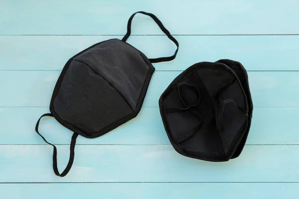 Black cotton mouth and nose mask to protect against flu and virus. Face mask during the coronavirus pandemic. Black face masks on a blue wooden background top view.