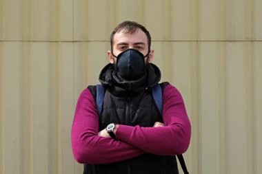 Sarı duvarın arka planında siyah maskeli adam. Korona virüsü salgını sırasında siyah sarısı ve yüz maskesi takan esmer adam. Virüs enfeksiyonuna karşı önlemler.