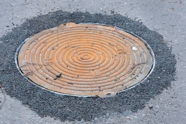 Asfaltın arka planında demir kapak. Paslı metal kapak yolda. Metal kapak hırsızlığı..