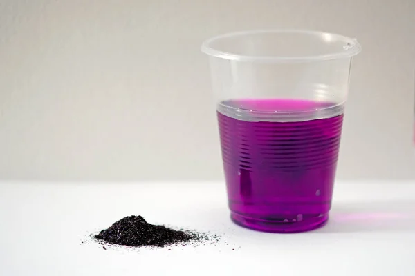 Beyaz arka planda potasyum permanganat tozu. Siyah toz potasyum permanganat ve gül suyu ile plastik bardak. Suda potasyum permanganat çözeltisi..