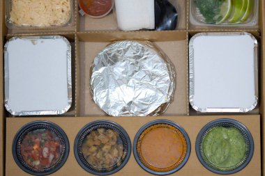 Yiyecek dolu plastik kaplarla dolu karton kutu. Eve tek kullanımlık sofra takımı olarak yemek teslimatı. Bir kafeden teslimat için yiyecek paketliyorum. Meksika yemekleri..