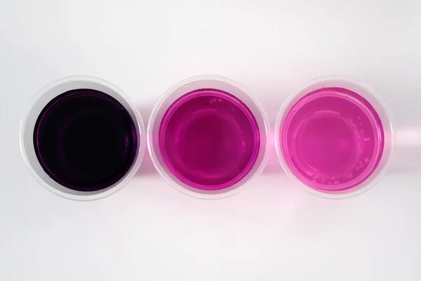 Beyaz arka planda potasyum permanganat. Plastik bardakta suyla birlikte siyah toz potasyum permanganat. Potasyum permanganatın farklı bir kalede suda çözümü.
