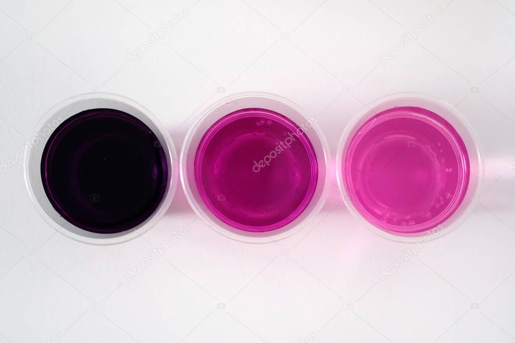 Potassium permanganate on a white background. Black powder potassium permanganate in a plastic glass with water. A solution of potassium permanganate in water different fortress