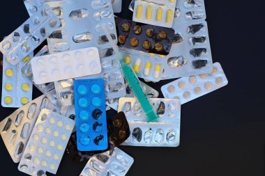 Siyah arka planda haplarla ambalaj. Haplardan oluşan su toplayıcı paketler. Bir sürü uyuşturucu ve iğneli yeşil bir şırınga. Hastalıkların tedavisi, eczanelerde ilaç fiyatlarında artış