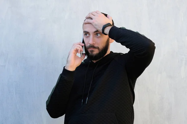 Adam telefonda gri bir duvara karşı konuşuyor. Adam telefonu kulağının yanında tutuyor ve diğer eliyle başını tutuyor. Telefondan kötü haberler, sürpriz, sıkıcı telefon konuşmaları.