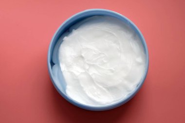 Yuvarlak bir kapta beyaz krema. Pembe arka planda bir kutuda vücut kremi. Yüz ve vücut bakımı, kozmetik ürünler..