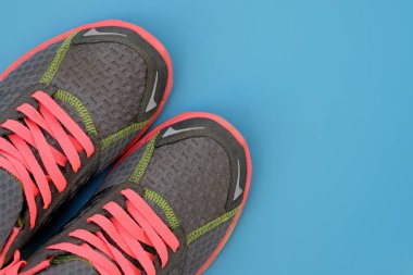 Mavi arka plan manzaralı pembe bağcıklı gri spor ayakkabılar. Renkli bağcıklı ve pembe tabanlı tekstil ayakkabılar. Aktif yaşam tarzı, spor, yarışmalar. Boşluğu kopyala