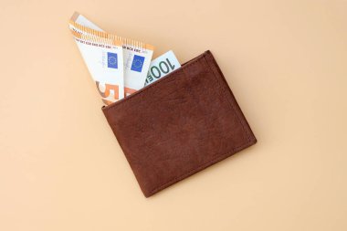 Üzerinde euro banknotları olan kahverengi deri cüzdan. Bej arka planda para olan kare bir cüzdan. Mali bağımsızlık kavramı, bütçenin korunması, ülkedeki ekonomik durum.