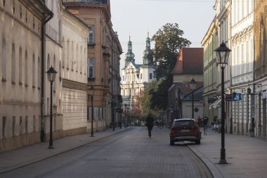Krakow, Polonya - Ağustos 2019: Grodska caddesi, eski Avrupa kentinin tarihi merkezi, sabah güneşinde Siena St. Bernardino Kilisesi manzaralı; yoldan geçenler kaldırıma çıkıyor.