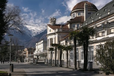 Merano / İtalya - Mart 2017: Arka planda Jugendstil Kurhaus binası ve karla kaplı dağlarla Passer Nehri 'ne paralel geçiş manzarası