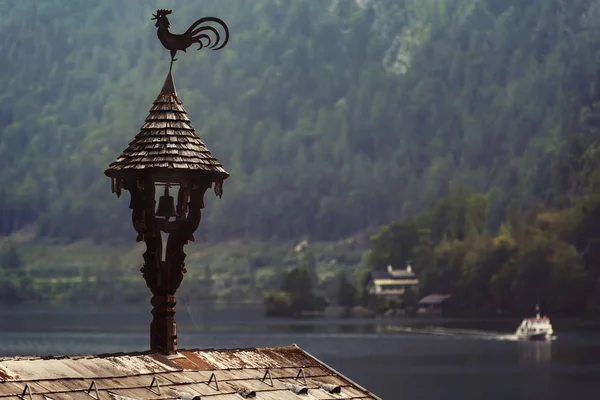 Paleta vieja en forma de gallo en una pequeña torre de madera en el techo de la casa temprano en la mañana contra los Alpes y el lago — Foto de Stock