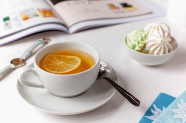 Limonlu beyaz çay, beyaz bir çarşafta beyaz bir çarşaf üzerinde mini krema ve resimli bir dergi, saat ve çay poşetleri. İyimser yaşam tarzı