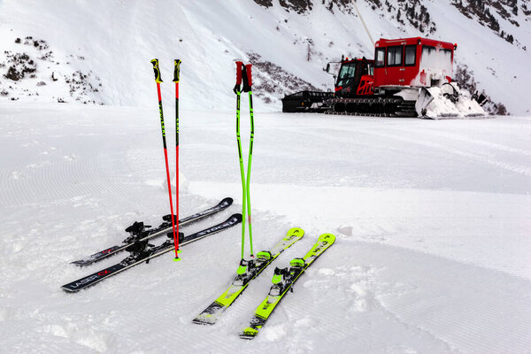 Ischgl, Austria - January 2020: Red machine for skiing slope preparations in Austrian Alps at background of mountains. Two pairs of skis and poles in the foreground