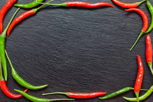 Fresh spicy red and green pepper on a slate board, various colorful chili peppers and cayenne peppers on dark background from above. Top view, copy space.