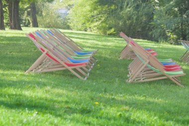 Parktaki iskemleler, güneş ışığı, yeşil çimenler.