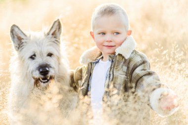 Mutlu gülümseyen sarışın çocuk çiftlikte köpek arkadaşıyla yürüyor.