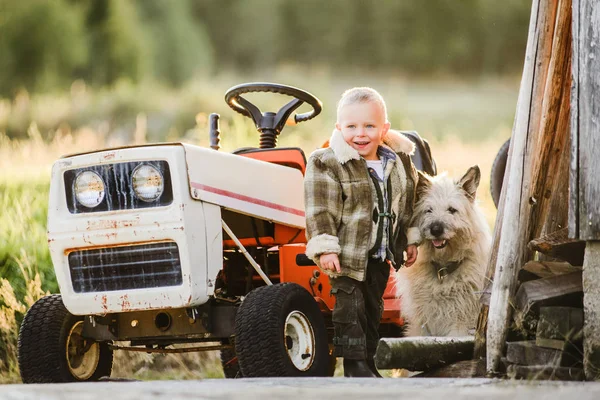 Loiro menino perto de cortador de grama cortador trator com cão amigo — Fotografia de Stock