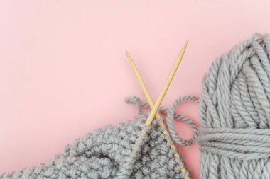 Bambu ahşap iğneler üzerinde gri örme kumaş parçası iplik topu ile, pembe arka plan üzerinde örgü süreci. Metin için alan kopyalama. Üst görünüm Düz döşeme Şablonu tasarımınız için