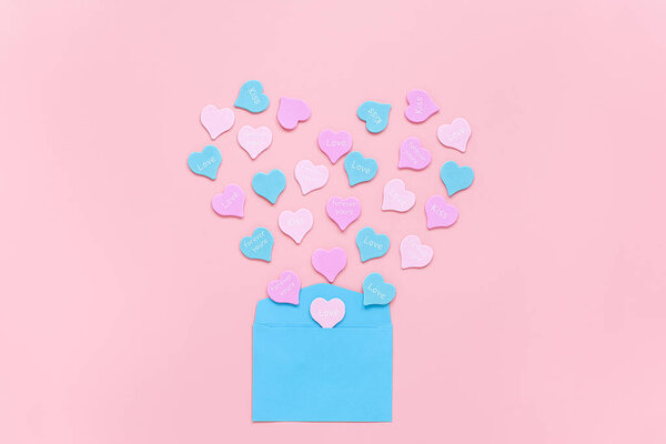 Красочные сердца с текстом ЛЮБОВЬ, ЦЕЛИ, НИКОГДА ВАШИ не вылетают в виде сердца из голубого бумажного конверта на розовом фоне. День святого Валентина концепция. Подарок для любовника. Признание в любви
