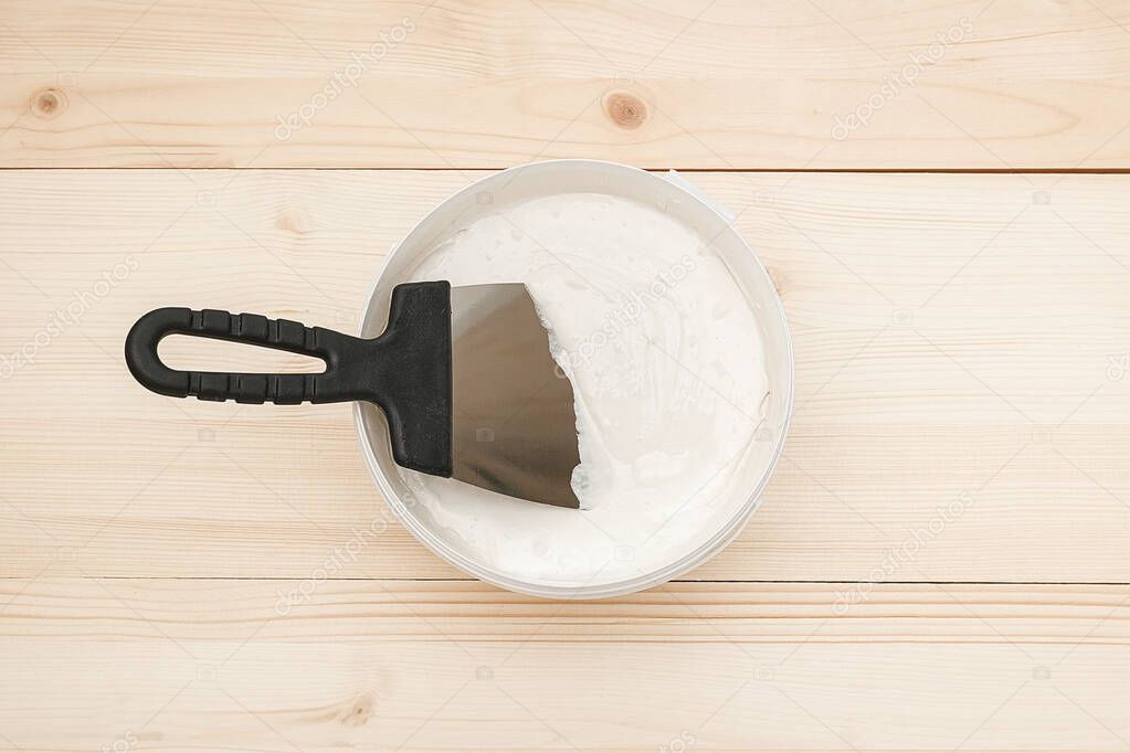 Spatula and a bucket of white putty on wooden boards. Top view Copy space