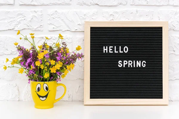 Κείμενο Γεια σας Άνοιξη σε μαύρο πίνακα επιστολών και μπουκέτο από χρωματιστά λουλούδια σε αστείο κίτρινο κύπελλο στο φόντο λευκό τοίχο από τούβλα. Concept Springtime διάθεση και ευτυχία — Φωτογραφία Αρχείου
