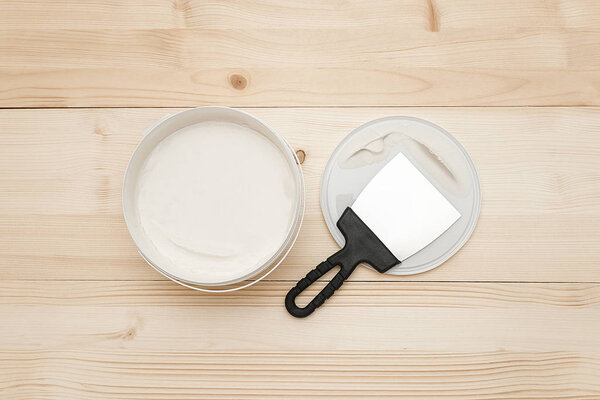 Spatula and a bucket of white putty on wooden boards. Top view Copy space