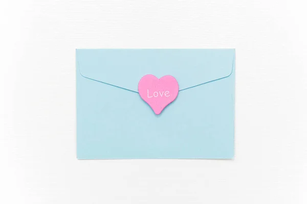 Love Letter. Blue closed envelope and pink heart with text LOVE on white background. Top view Flat lay Template for your text. Valentines day, Mothers day, Womens day greeting card