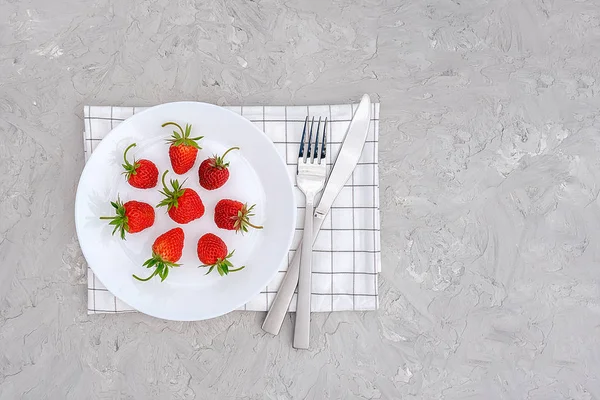 stock image Red ripe strawberries berry on white plate, cutlery and red alarm clock on gray stone background table. Top view, flat lay, copy space Template. Concept diet and detox time or summer menu time