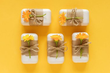 El yapımı doğal sabun seti. El işi kağıt, kırbaç ve sarı arka planda turuncu takvim çiçekleriyle süslenmiş. Organik kozmetik, sıfır atık, çevre dostu konsept. Üst Görünüm Düz yatay Boşluğu Kopyala