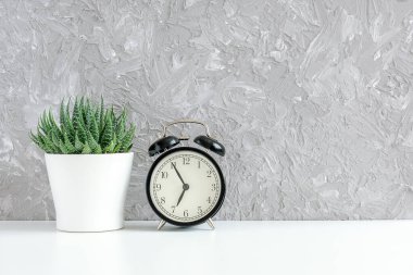 Siyah alarm saati ve gri beton duvarın arkasındaki masada beyaz tencerede yeşil sulu. Sabah 5 'ten 7' ye kadar. İyi sabahlar. Anlaşıldı.