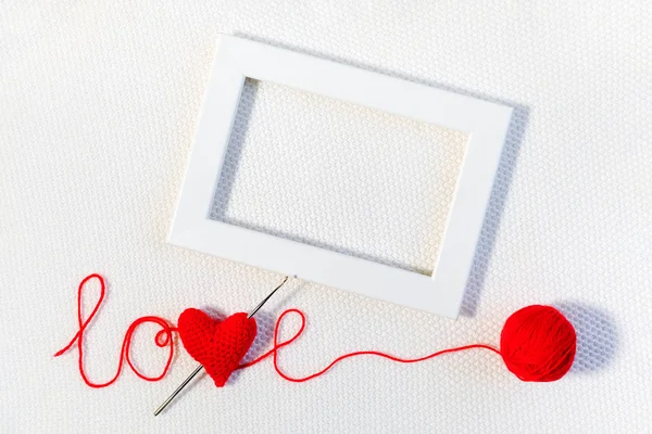 San Valentino o sfondo di nozze. Cuore di volume rosso lavorato a maglia in amore di parola, palla di filo e cornice bianca su sfondo lavorato a maglia. Modello per design, biglietto da visita, invito. Mock up Vista dall'alto — Foto Stock