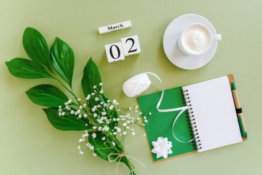 Tahta küplerin takvimi 2 Mart. Boş not defteri, bir fincan kahve, yeşil arka planda buket çiçekleri. Merhaba yay üst görünüm düz yatay konsept