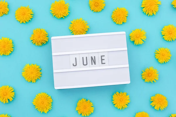 Text June on light box and yellow dandelions on blue background. Concept hello summer. Top view Flat lay — Stock Photo, Image