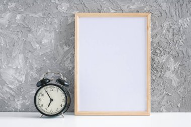 Ahşap, beyaz, boş bir çerçeve ve gri beton arka plandaki masada siyah alarm saati. Dizaynınız için Mockup Şablonu