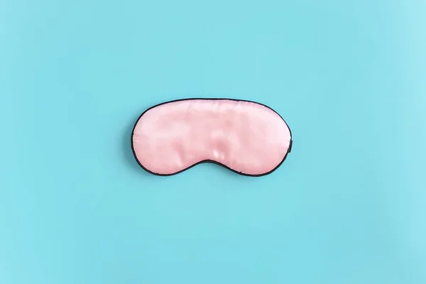 Pink silk sleep mask for eyes on a blue background. Top view Flat lay Copy space. Concept eye protection from light for good sleep and melatonin production