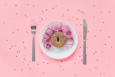 Gözü ve saçı tabakta santimetre bantlı, çatal bıçak takımı pembe arka planda olan bir kadının soyut komik yüzü. Fast food, şişmanlatıcı ve sağlıksız yeme yaratıcılık konsepti Top view