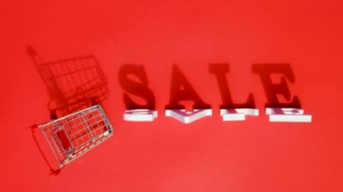 Küçük boş alışveriş arabası, kelime satışı ve düşen beyaz harflerin kırmızı arka planda büyük bir gölgesi var. Konsept satışı. Metin, tasarım, reklam veya reklam için yaratıcı şablon